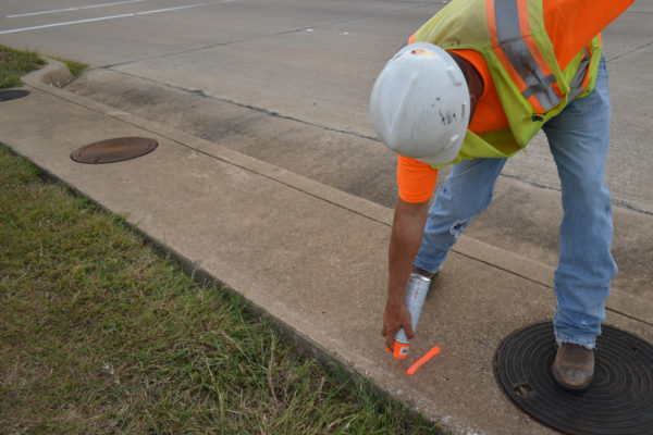 Surveyor Marking The Sidewalk While Wearing A Hard Hat And Safety Vest Orange Marking Paint